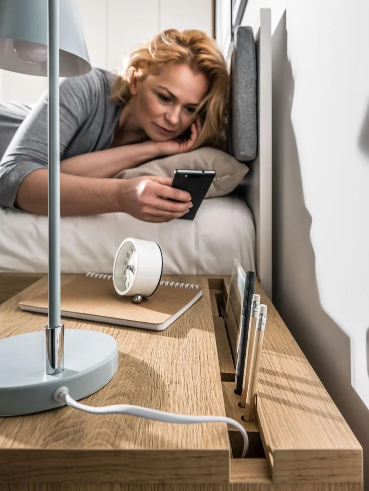 Kobieta sięga z łóżka po telefon
